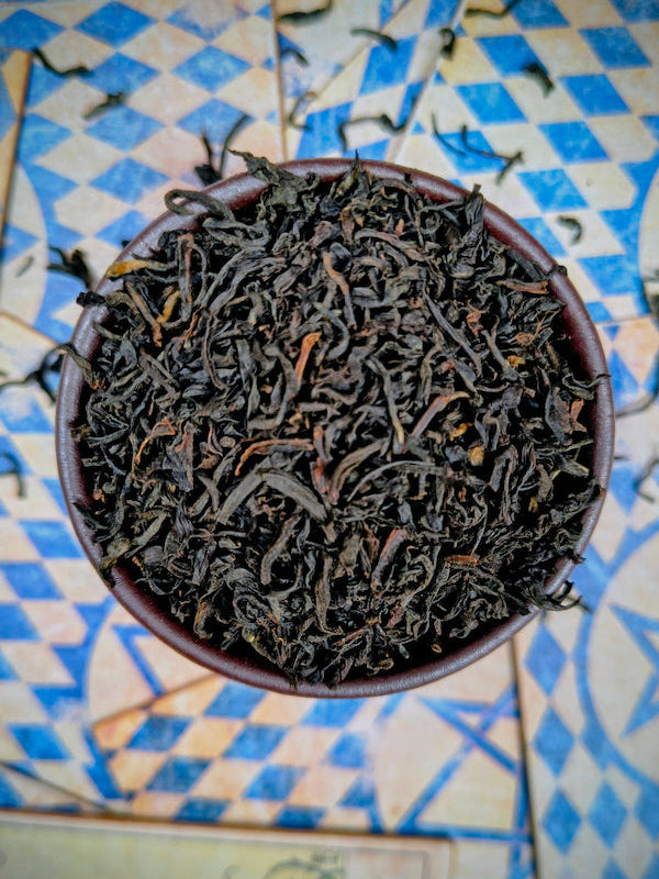 Dry black tea leaves in a small bowl on a patterned surface