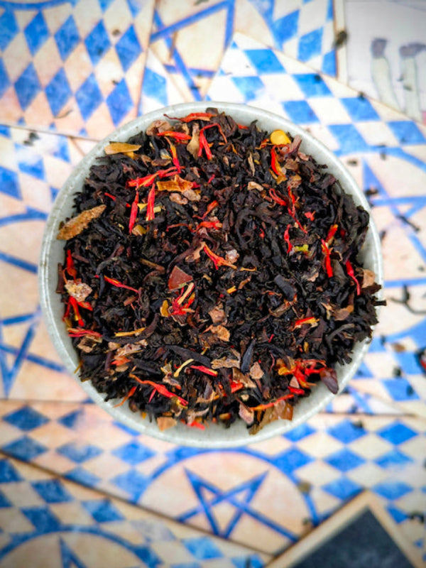 Tea leaves with red and orange elements in a white bowl on a blue and white patterned surface.